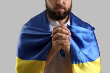 Ukrayna bayrağı taşıyan genç adam gri arka planda dua ediyor, yakın plan