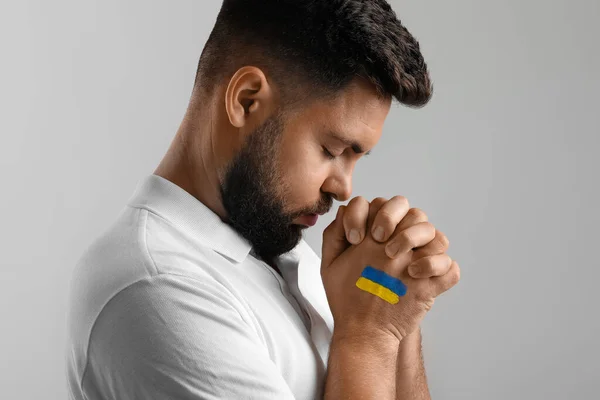 Young man with drawn flag of Ukraine praying on grey background, closeup