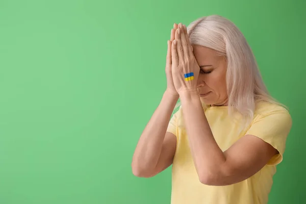 Mature woman with drawn flag of Ukraine praying on green background