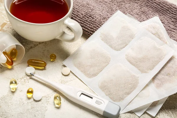 Mustard plasters with pills, thermometer, cup of tea and towel on grunge background, closeup
