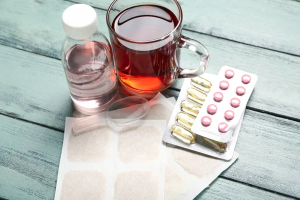 Mustard plasters with cup of tea, pills and cough syrup on color wooden background