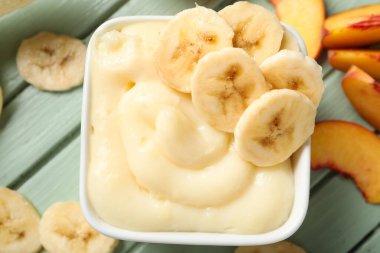 Bir kase lezzetli vanilyalı puding ve muz renkli ahşap masa, yakın plan