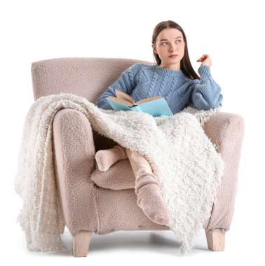 Beyaz arka planda rahat koltukta ekose kitap okuyan genç bir kadın.