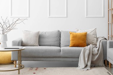 Aydınlık oturma odasında yastıklı ve ekoseli rahat bir kanepe.