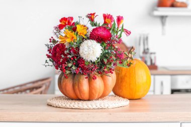 Mutfakta tezgahta sonbahar çiçekleri olan balkabağı.