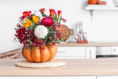 Mutfakta tezgahta sonbahar çiçekleri olan balkabağı.