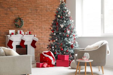 Oturma odasının içinde Noel çantası, şömine ve Noel ağacı var.