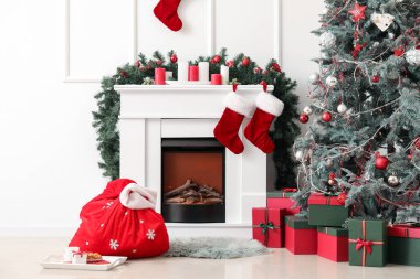 Noel Baba çantası, şömine ve Noel ağacıyla aydınlık oturma odasının içinde.