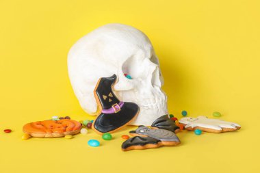 Tatlı Cadılar Bayramı kurabiyeleri ve sarı arka planda insan kafatası.