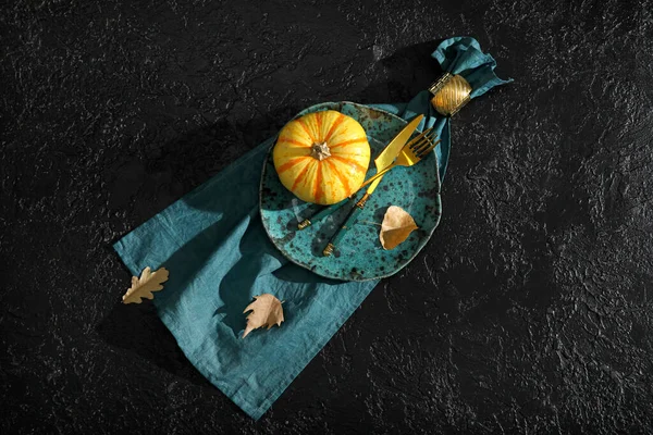 Autumn table setting with pumpkin and fallen leaves on black background