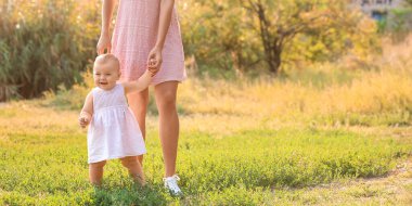 Anne küçük bebeğine dışarıda yürümeyi öğretiyor.