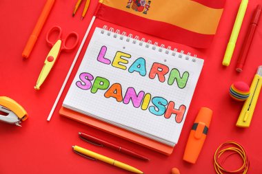 Notebook with text LEARN SPANISH, flag and stationery supplies on red background clipart
