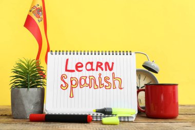 Not defterinde LeARN SPANISH, kırtasiye, saksı, kupa, bayrak ve alarm saati var.