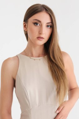 Beyaz arka planda zarif bej elbiseli güzel, modaya uygun genç bir kadın.