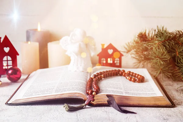 Open Holy Bible with prayer beads and angel toy on table. Christmas story