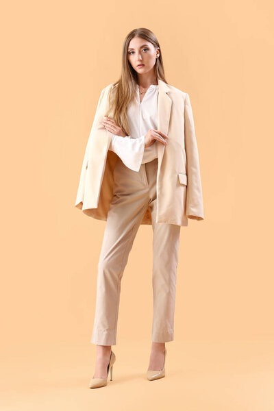 Красивая модная молодая женщина в элегантном костюме на бежевом фоне