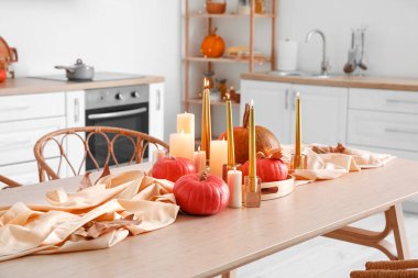 Kabaklı yemek masası, düşmüş yapraklar ve hafif mutfakta yanan mumlar.