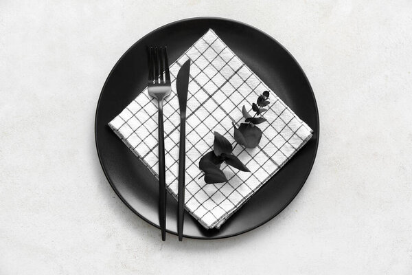 Черная тарелка с салфеткой и столовыми приборами на светлом фоне