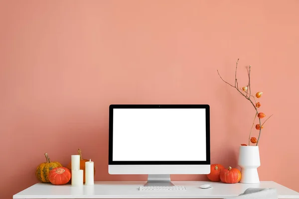 Workplace with computer, candles and pumpkins near pink wall