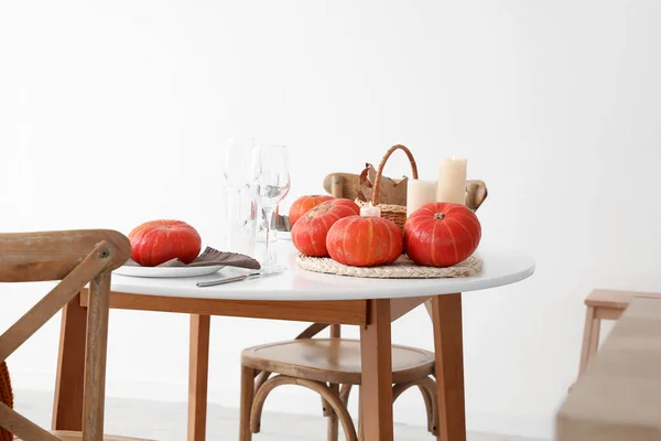 Basket with fallen leaves, pumpkins and burning candles on dining table in kitchen
