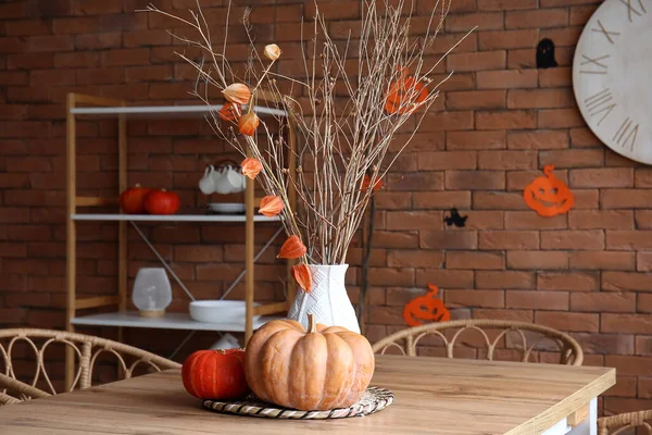 Vase with tree branches and Halloween pumpkins on dining table in kitchen