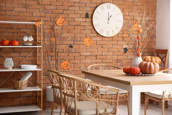 Vase with tree branches and Halloween pumpkins on dining table in kitchen