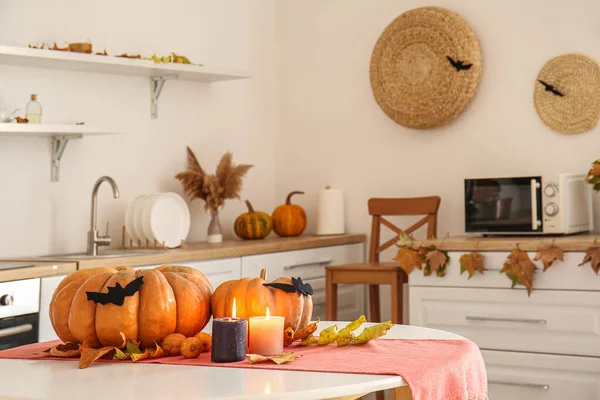 Halloween pumpkins with fallen leaves and burning candles on dining table in kitchen