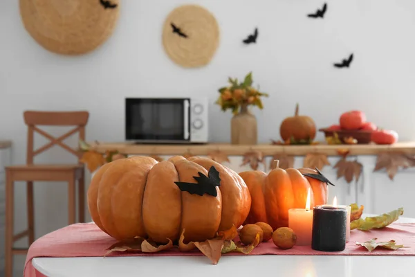 Halloween pumpkins with fallen leaves and burning candles on dining table in kitchen