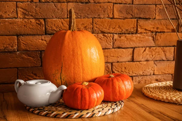 Halloween pumpkins and teapot on dining table near brick wall