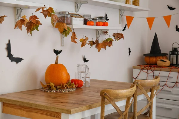 Dining table with Halloween pumpkins, leaves and glasses of water in kitchen