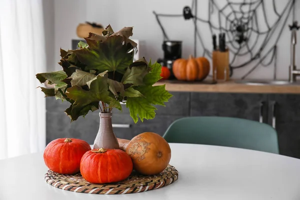 Vase with fallen leaves and Halloween pumpkins on dining table in kitchen