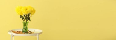 Taze kasımpatı çiçekli vazo ve sonbahar yaprakları masanın üzerinde sarı arkaplan ile metin için boşluk.