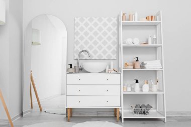 Modern lavabo, büyük ayna ve farklı banyo aksesuarlarıyla banyo içi beyaz duvarın yanında.