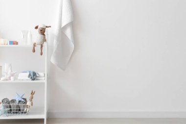 Çocuklar için banyo malzemeleri ve banyoda beyaz duvarın yanında oyuncaklar olan raf ünitesi.