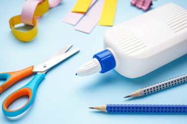 Mavi arka planda kalem ve makaslı bir şişe yapıştırıcı, yakın plan.