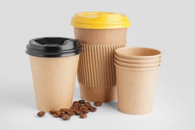 Beyaz arka planda paket kâğıt bardak ve kahve çekirdekleri.