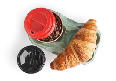 Kahve çekirdekli kağıt bardaklar ve beyaz arka planda kruvasan.