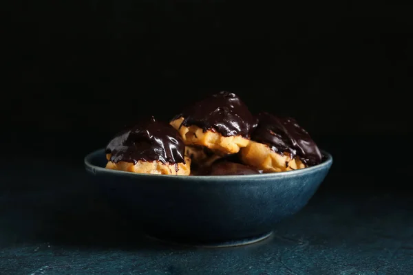 Bowl of delicious eclairs on dark color background