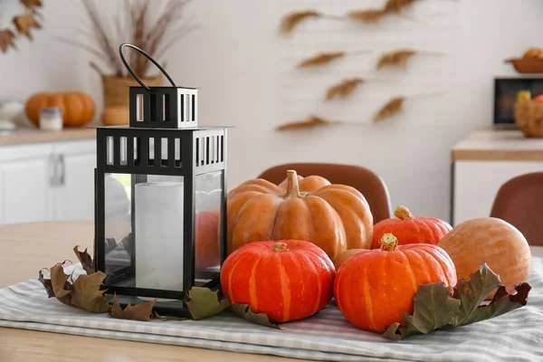 Halloween pumpkins with lantern and leaves on dining table in kitchen