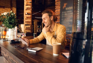 Kafesinde tablet bilgisayarla çalışan genç bir işletme sahibi.