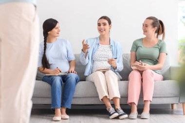 Hamile ve not defterleri olan genç kadınlar hamile anneler için koltukta oturuyorlar.