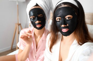 Yatak odasında aktif kömür çarşaflı yüz maskeleri olan güzel genç kadınlar.