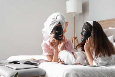 Yatak odasında aktif kömür çarşaflı yüz maskeleri olan güzel genç kadınlar.