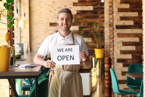 Handsome business owner with opening sign in his cafe
