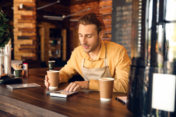 Young business owner with cup of coffee using calculator in his cafe