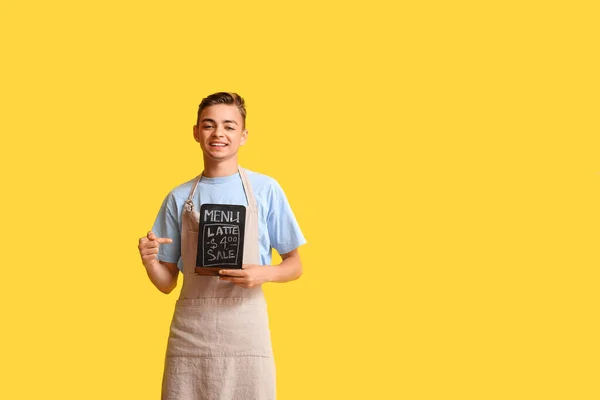 Male barista pointing at chalkboard with menu on yellow background