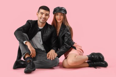 Pembe arka planda, sonbahar elbiseli şık genç bir çift.