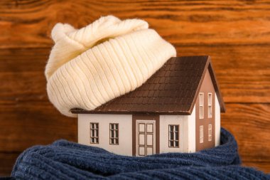 Koyu ahşap arka planda örülü şapka ve eşarplı ev modeli. Isıtma kavramı