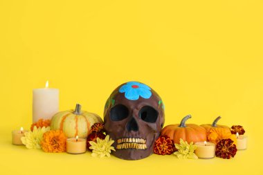 Meksika Ölüler Günü için boyanmış kafatası (El Dia de Muertos), sarı arka planda çiçekler, mumlar ve balkabakları