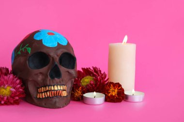 Meksika Ölüler Günü için boyanmış kafatası (El Dia de Muertos), pembe arka planda mumlar ve çiçekler